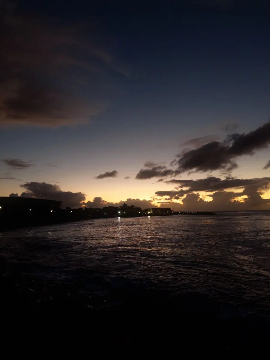 Sunset over dark water, clouds lit orange at the horizon