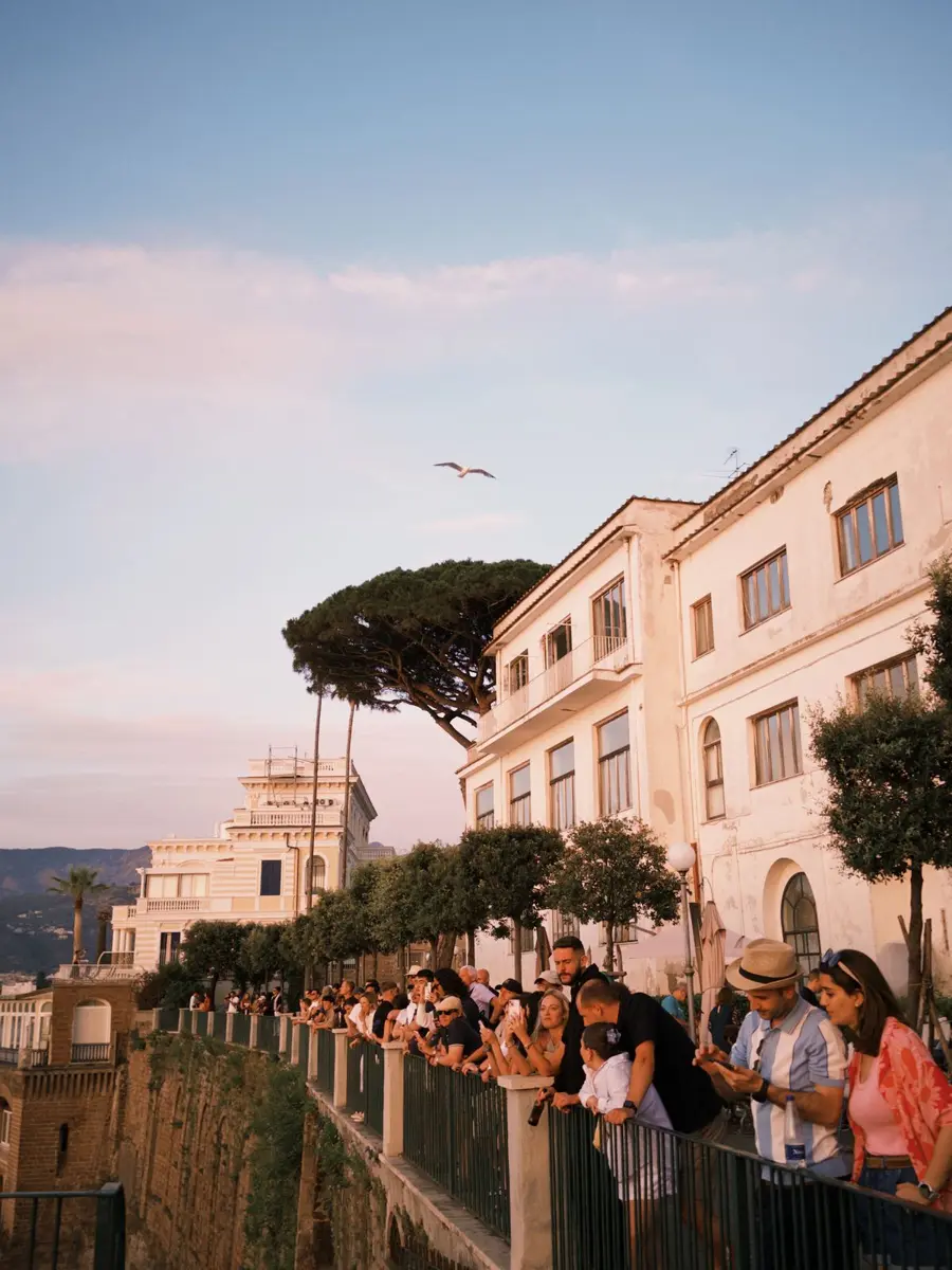 People lining a cliffside promenade in golden evening light