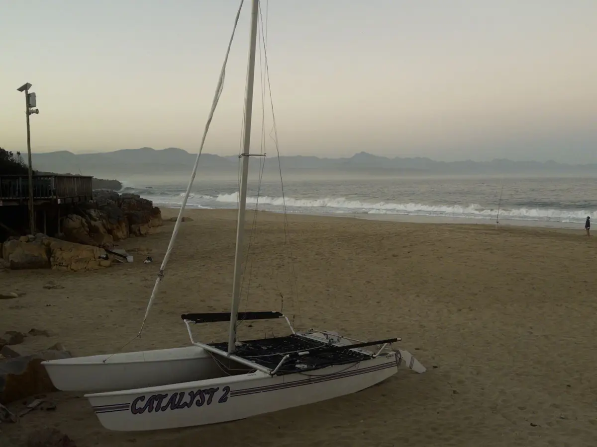 A catamaran pulled up on a beach at dusk